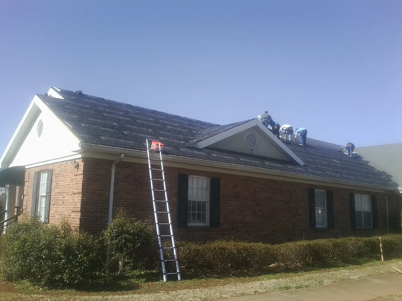 Crew tearing shingles off a brick ranch roof with a ladder set — Emergency Roof Repair work by our crew in Branchport