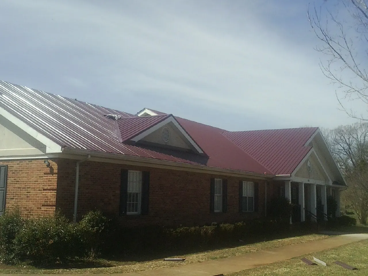 Red metal roof with gabled entries on a long brick building, from a Hail Damage Roof Repair job in Branchport