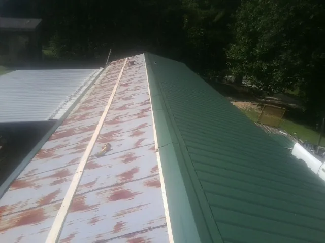 Old rusted panels beside newly installed green metal roofing — Wind Damage Roof Repair by Roofing Brothers in Branchport