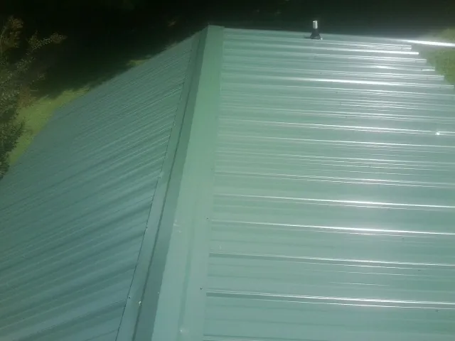 New green metal panels meeting at the ridge of a roof — Flat Roof Repair work by our crew in Branchport