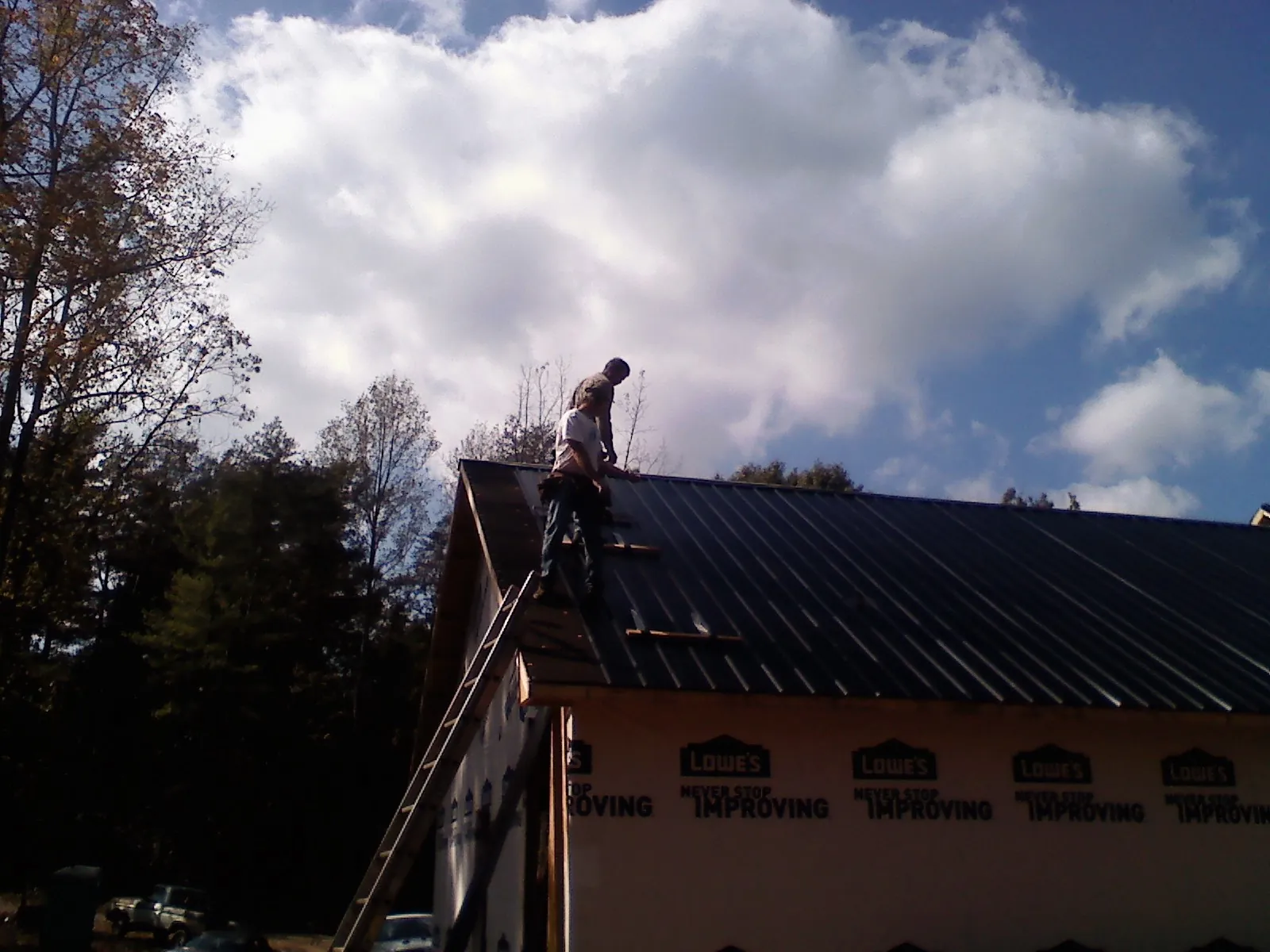 Roofer fastening dark metal panels high against a cloudy sky, from a Roof Inspection job in Branchport