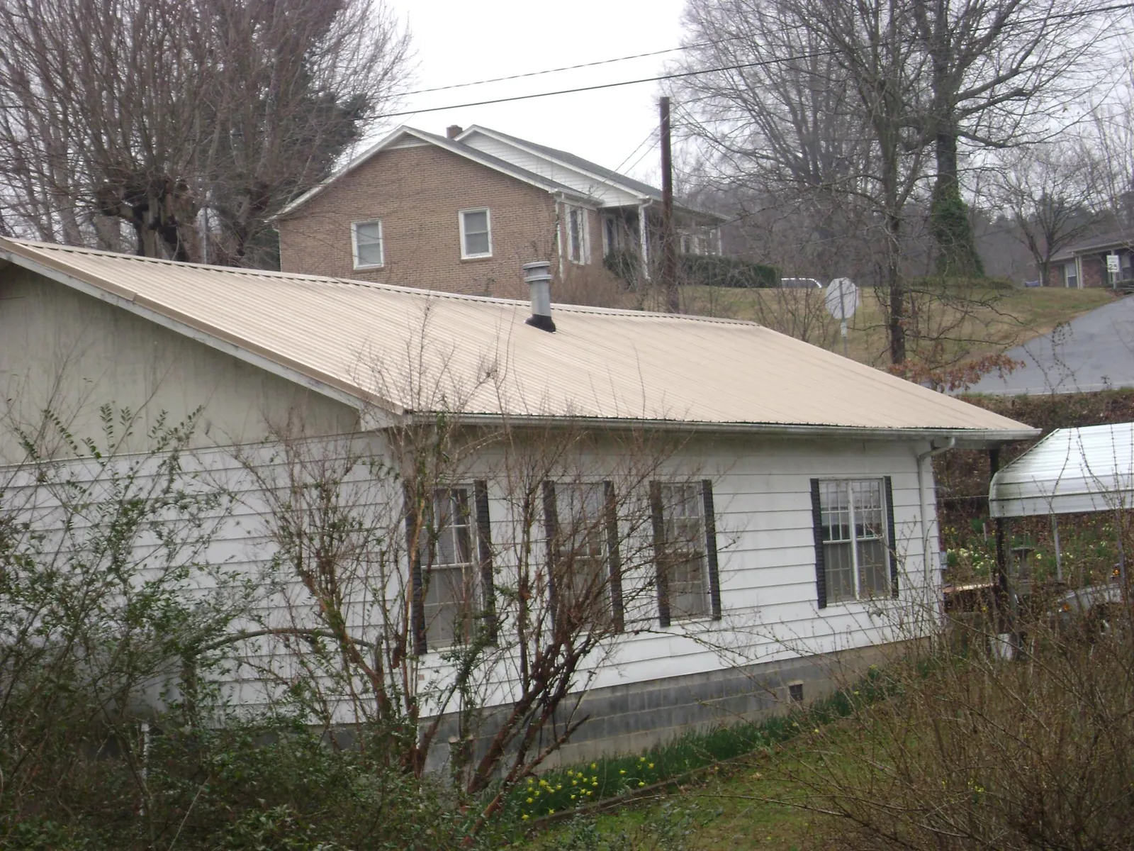 Tan metal roof on a white sided house set into a hillside — Commercial Roofing by Roofing Brothers in Branchport
